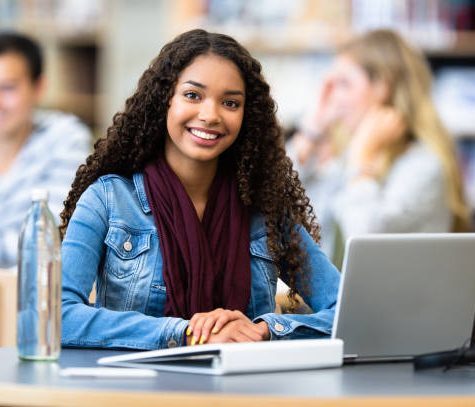 istockphoto-1214546578-612x612 A young African American female student sits and works on her laptop in the library of her school.